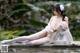 A woman in a white lingerie sitting on a ledge next to a pool.