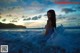 A woman in a blue dress sitting in the ocean at sunset.